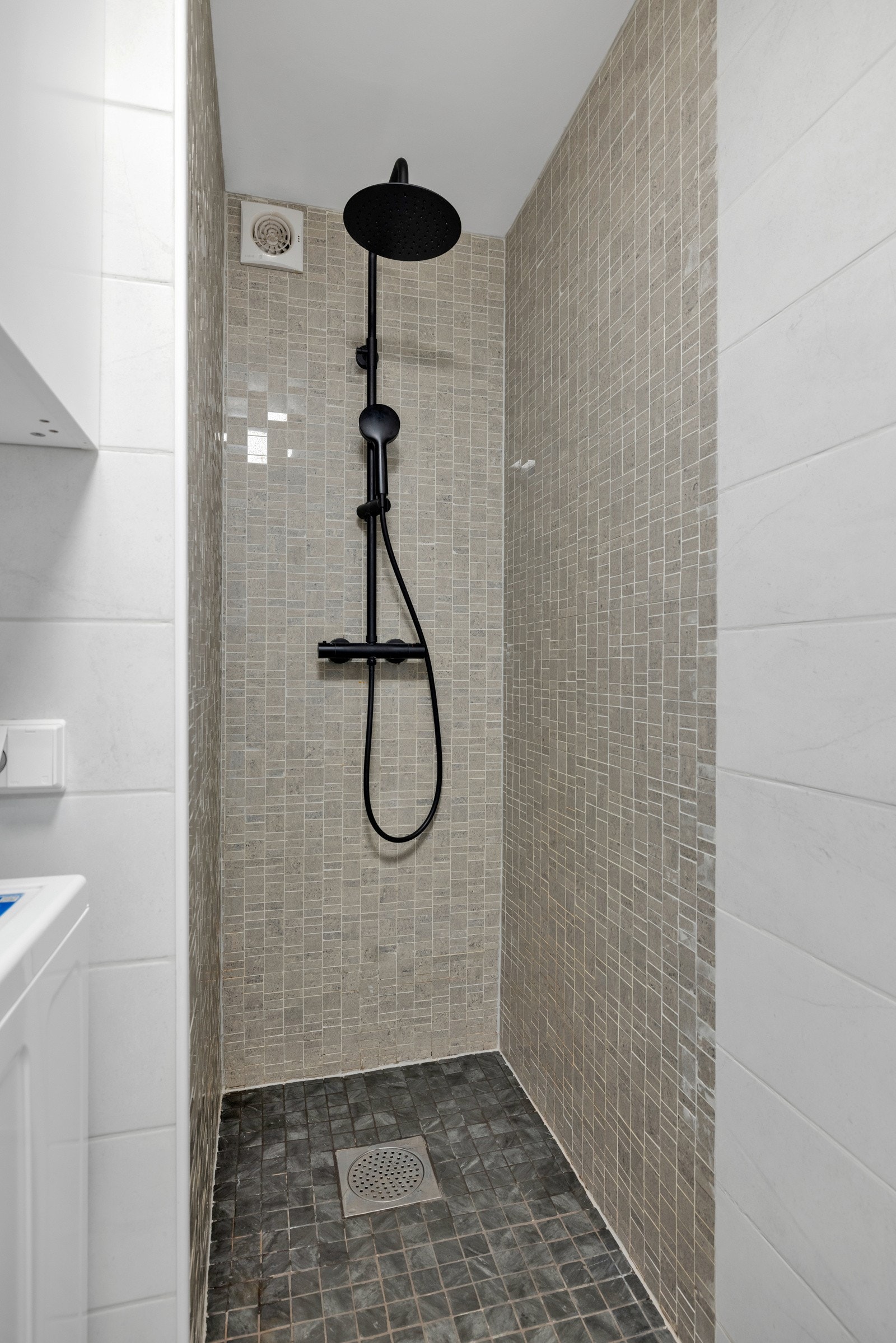 Dusjnisjen har mosaikkfliser på gulvet og veggene, og sort blandebatteri med både hånddusj og regndusj Galleribilde