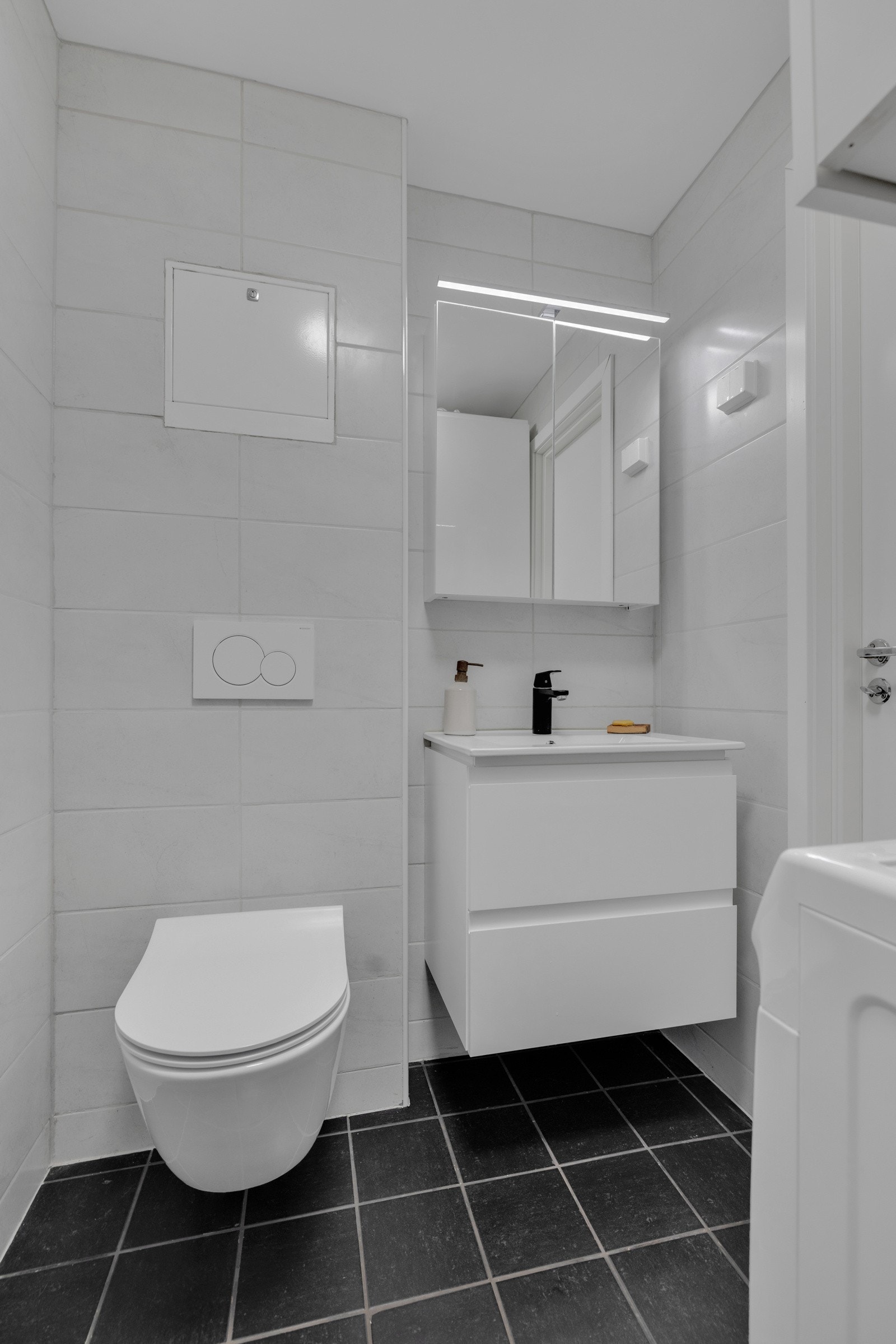 Badet er innredet med vegghengt toalett og et baderomsmøblement som består av et overskap, skuffeseksjon med heldekkende servant og et speilskap med belysning Galleribilde