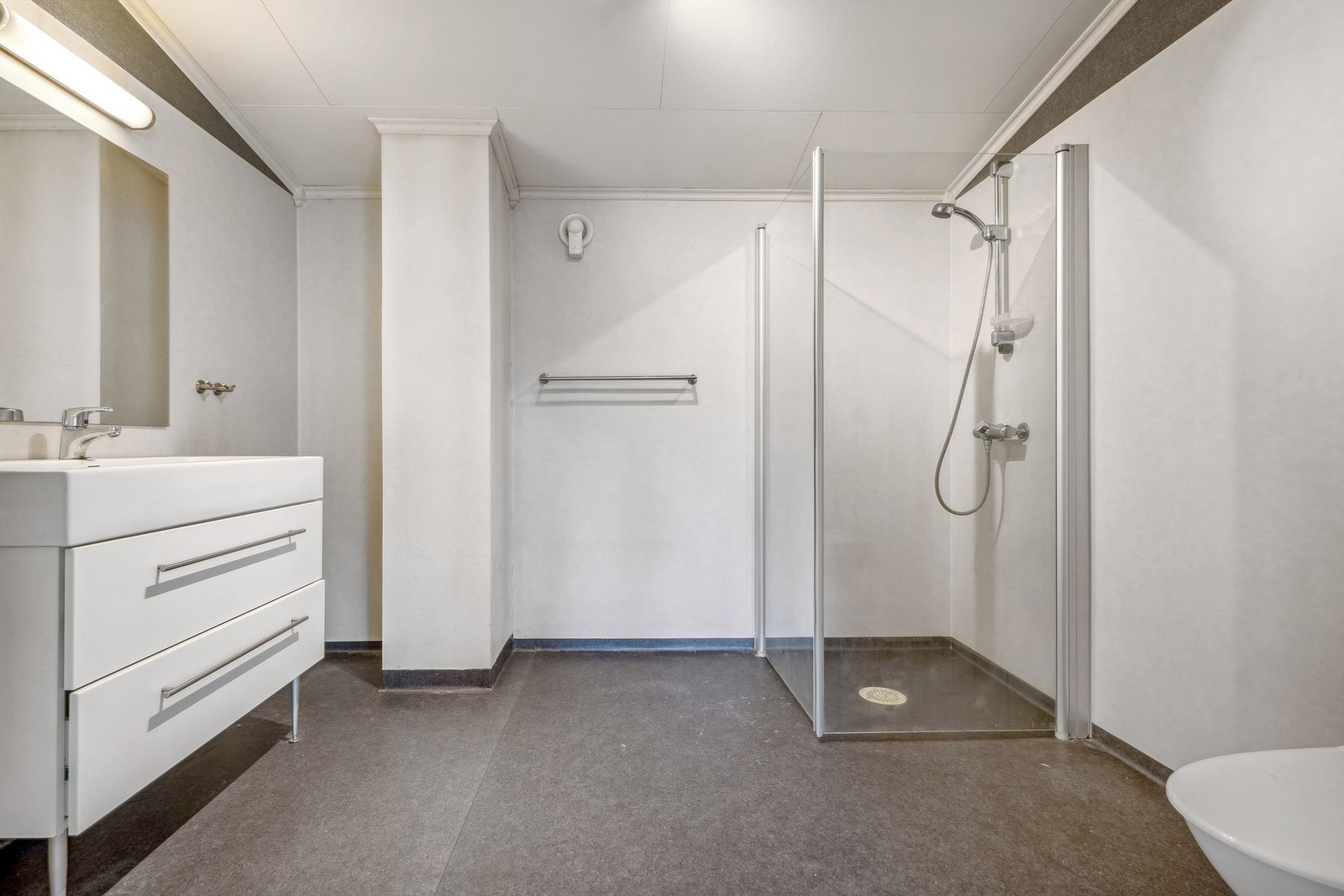 Baderommet i 2. etasje med grått vinylbelegg på gulvet og lysgrått belegg på veggene. Badet er innredet med nedfelt servant i lys skuffeinnredning, speil, dusjhjørne med dusjarmatur montert på vegg og dører og gulvmontert toalett. Galleribilde