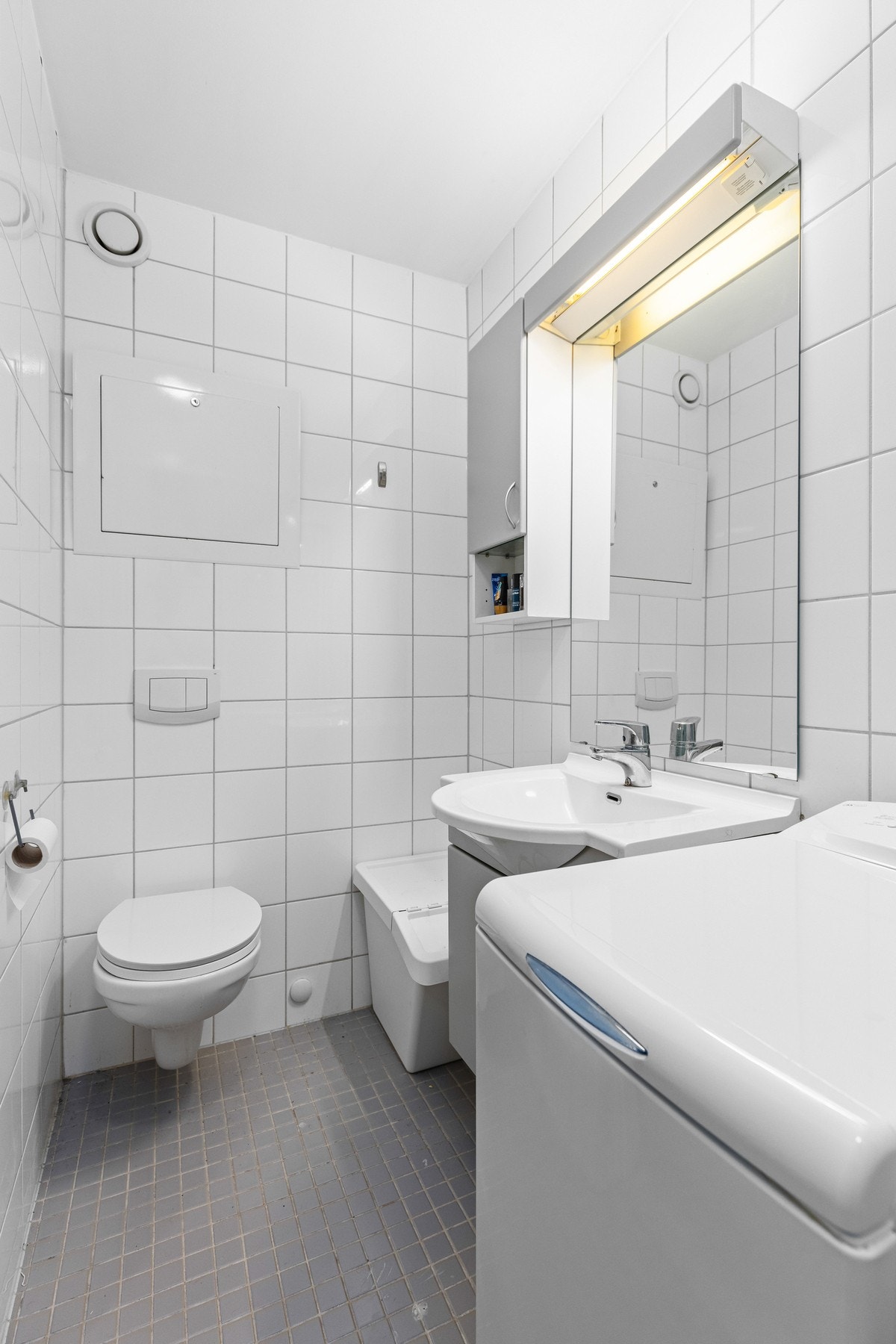 Badet har flislagt gulv og vegg, samt en servant på et underskap og et speil. Galleribilde