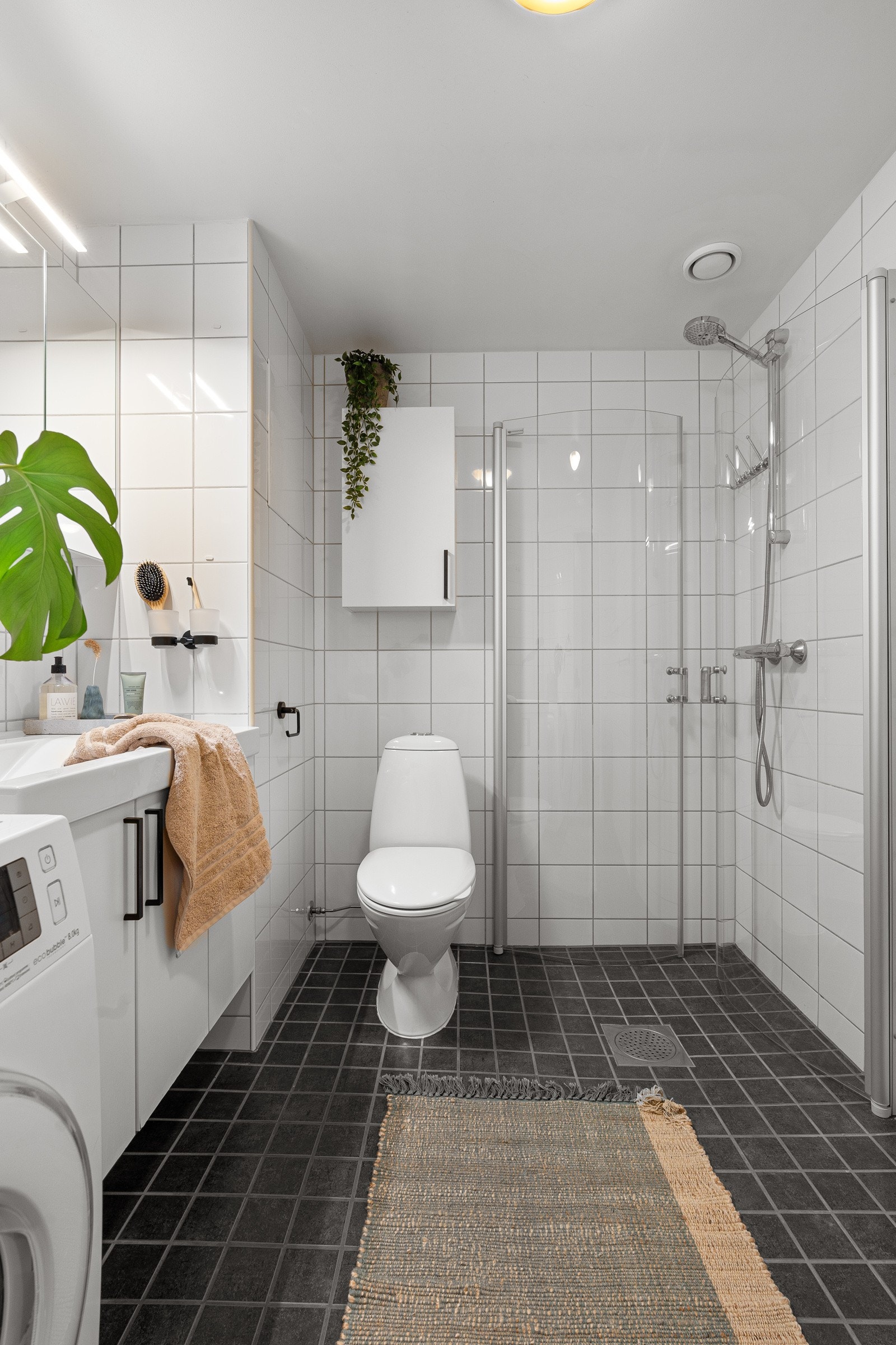 Badet er flislagt med varme i gulv og utstyrt med wc, dusjhjørne med innfellbare glassdører og opplegg for vaskemaskin. Galleribilde
