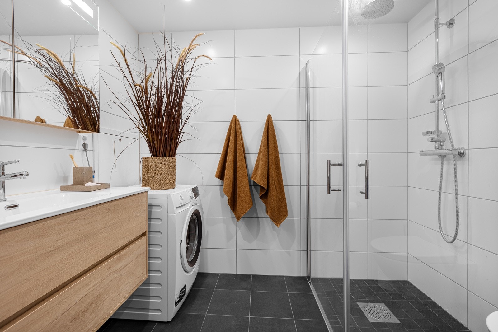 Lekkert flislagt bad med elektiske varmekabler i gulv. Badet er innredet med vegghengt wc, dusjhjørne med innfellbare glassdører, opplegg for vaskemaskin samt servant med underskap og speilskap. Downlights i tak. Galleribilde