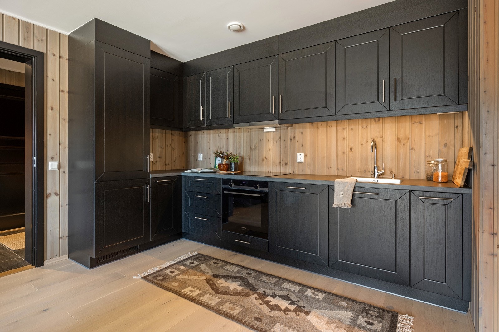 Flott kjøkken i L-form med god skap- og benkeplass. Innredning med både over- og underskap med fronter i sort utførelse. Integrerte hvitevarer med komfyr, platetopp, avtrekksvifte, oppvaskmaskin og kjøl/fryseskap. Galleribilde