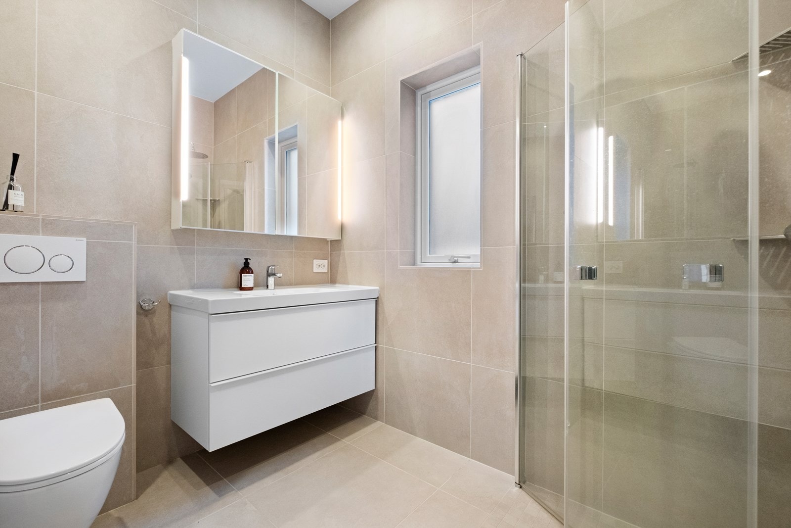 Flott bad i første etasje med flis og varmekabel på gulv og flis på vegger. Dusjhjørne med glassdører, veggmontert toalett og hel servantplate med underskap. Ventilasjon i himling. Galleribilde