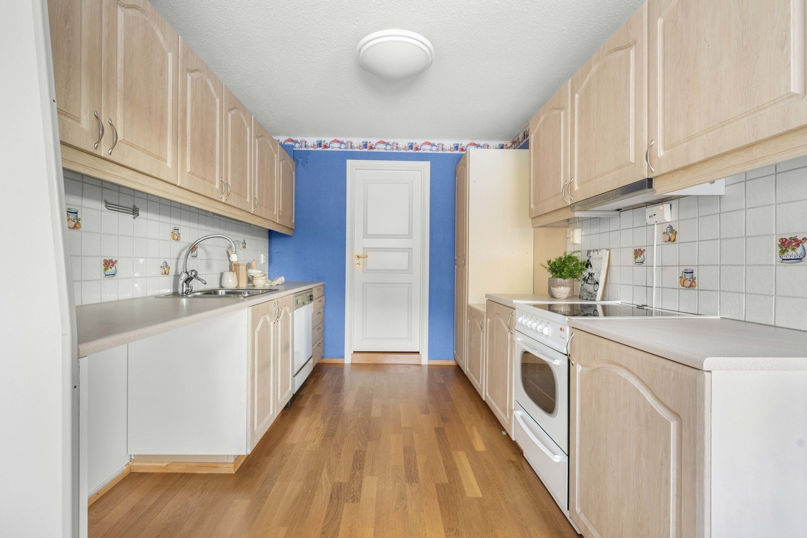 Kjøkkeninnredningen har profilerte fronter og benkeplate i laminat med nedfelt oppvaskkum. Det er fliser på veggen mellom kjøkkenbenken og overskapene, samt benkeskapsbelysning og stikkontakter under overskapene Galleribilde