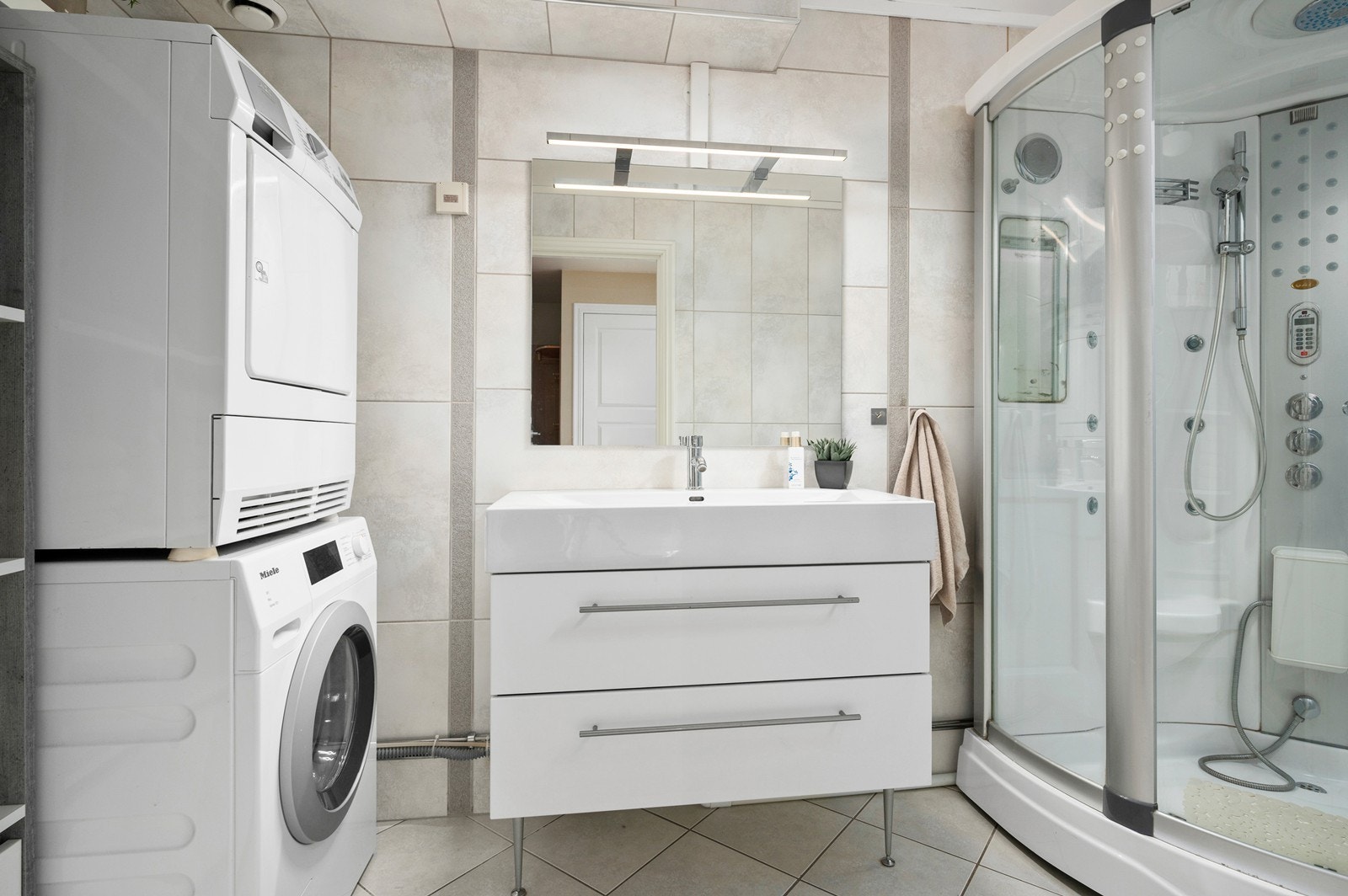 Baderom med flislagt gulv og vekker. Lys baderomsinnredning og opplegg for vaskemaskin, Galleribilde