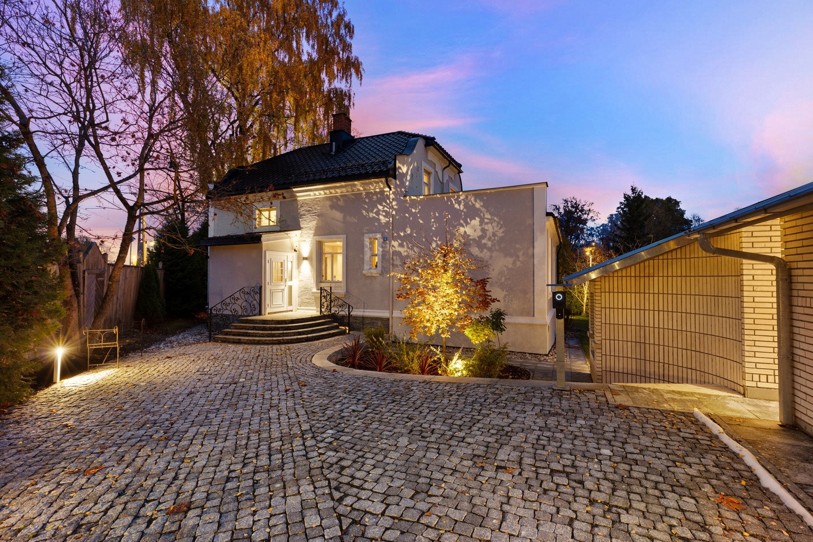 Innkjørselen inn til huset er brosteinsbelagt. Elbil lader i garasje og på ladestolpe på gårdsplassen Galleribilde