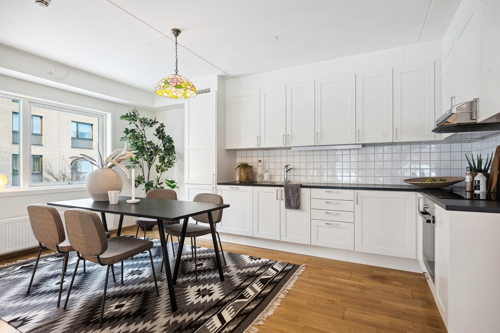 Lys og romslig kjøkken med fliser på vegg og belysning under overskap Galleribilde