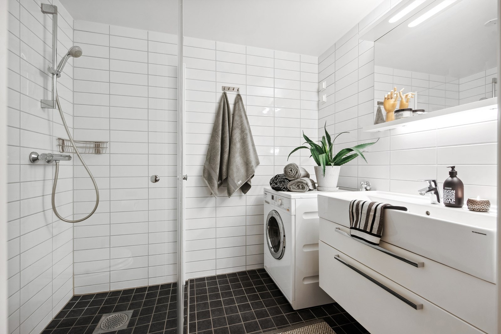 Lekkert baderom utstyrt med vegghengt toalett, dusjhjørne med glassdører, heldekkende servant med tilhørende servantinnredning Galleribilde