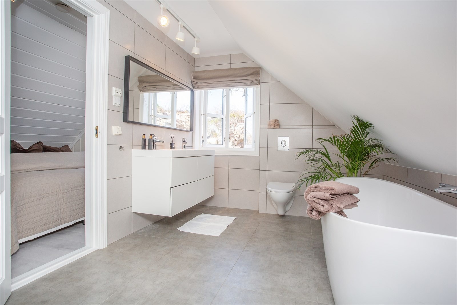 Badet er flislagt på gulv og vegg, baderomsinnredning med skuffeseksjon, veggheng toalett, badekar og dusj Galleribilde