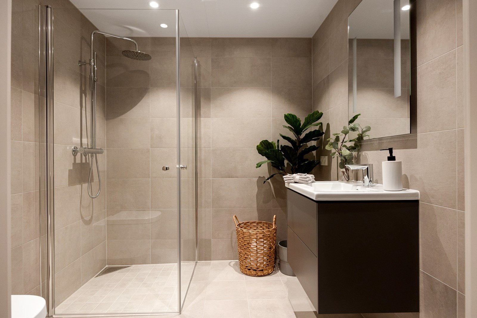 Delikat sandfarget flislagt baderom med vannbåren gulvvarme og downlights i himlingen. Dusjhjørne med innfellbare dusjvegger i herdet glass og regnfallsdusj. Galleribilde