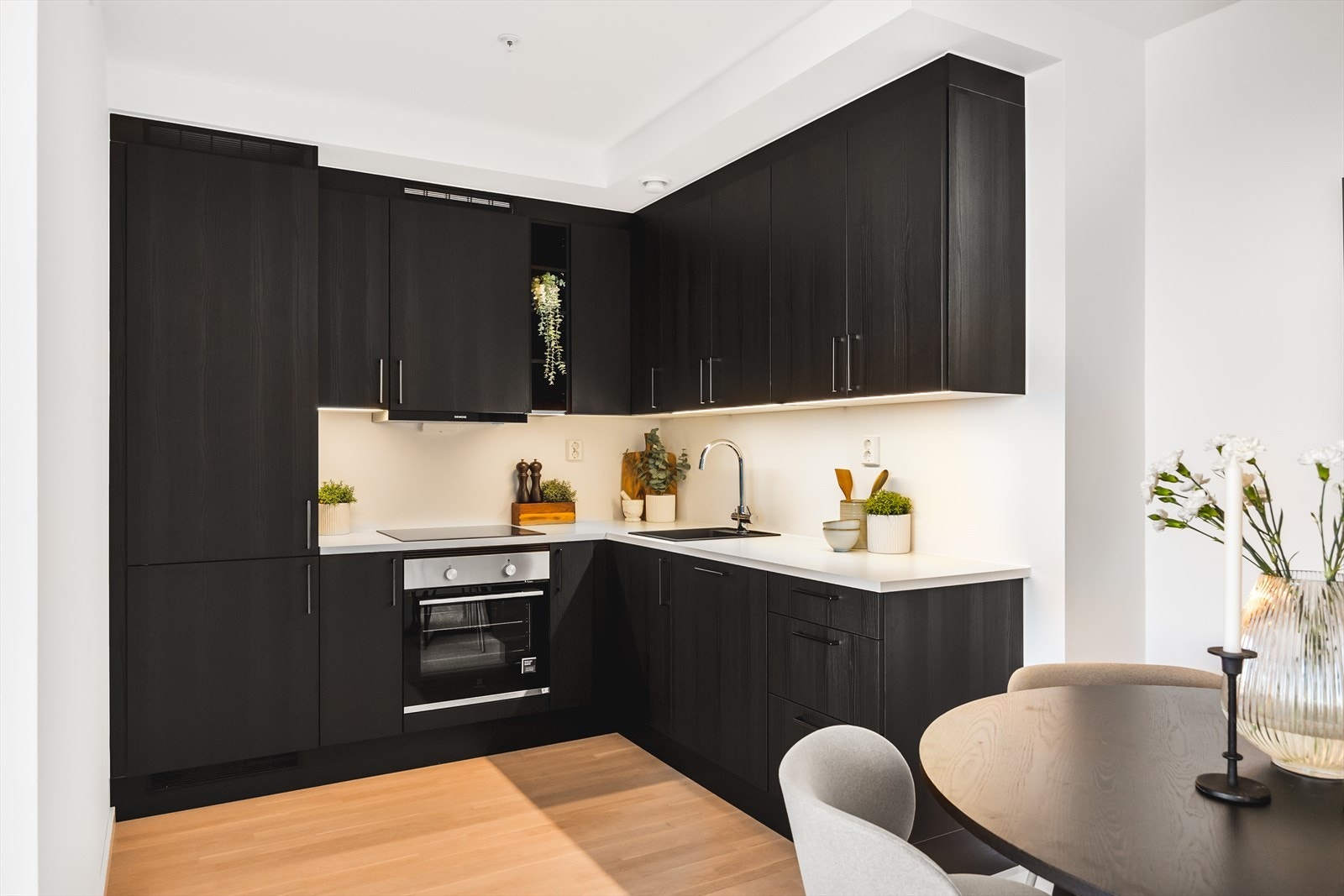 Moderne HTH-kjøkken med god skap- og benkeplass. Kjøkkenet har sorte fronter, benkebelysning under overskap og kjøkkenventilator (iQ300). Hvitevarene er integrerte og består av: stekeovn, platetopp, oppvaskmaskin og kombiskap. Galleribilde