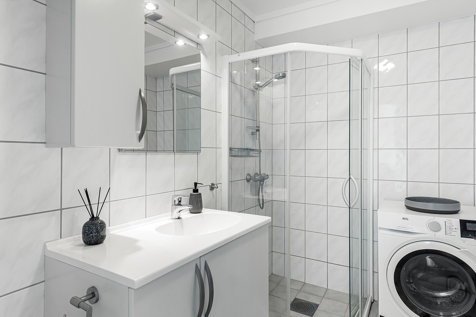 Badet har hvite veggfliser, grå gulvfliser, gulvvarme og mekanisk avtrekk. Galleribilde