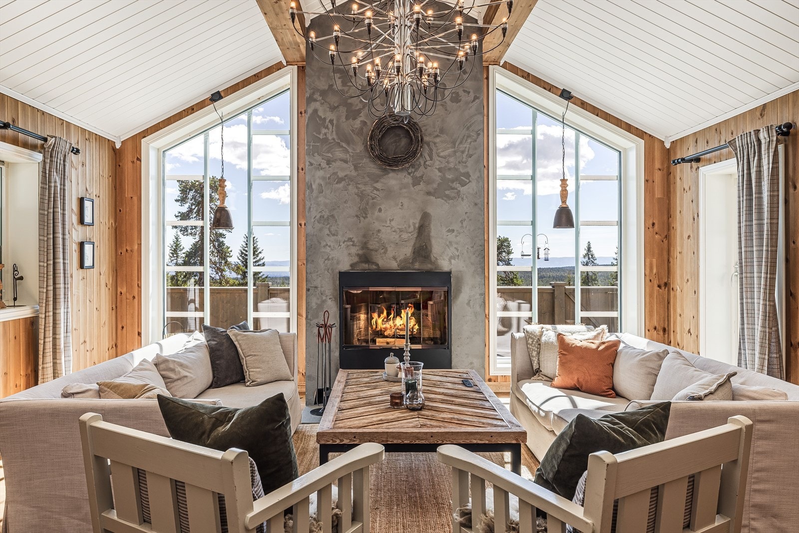 I dag er stuen innredet med en romslig sofagruppe foran peisen. Kombinasjonen med takhøyden og vinduene i rommet gjør at du får naturen og utstikten tett innpå. Et rom som må oppleves. Galleribilde