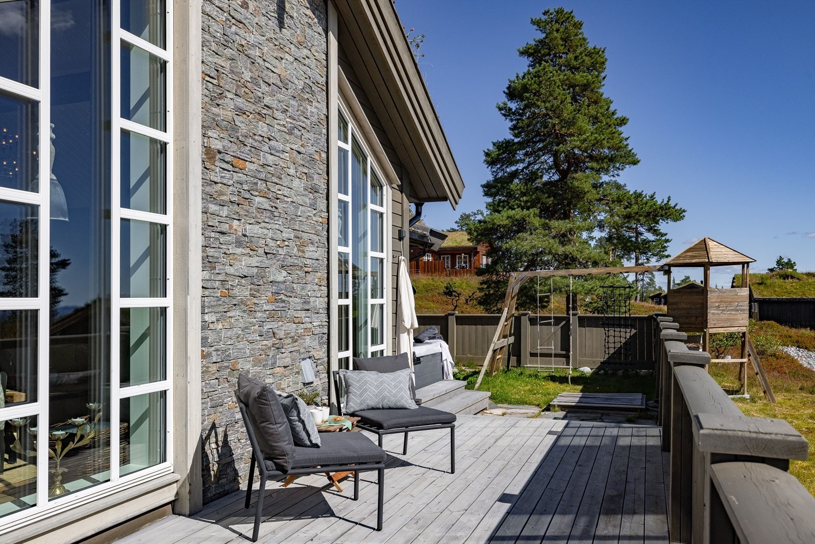 Langs utevegg ved stue er det en flott steinvegg som gir et lekkert og stilfult preg på hytta sin fasade. Merk også den tilrettelagte lekeplassen for de yngste i enden av terrassen. Galleribilde