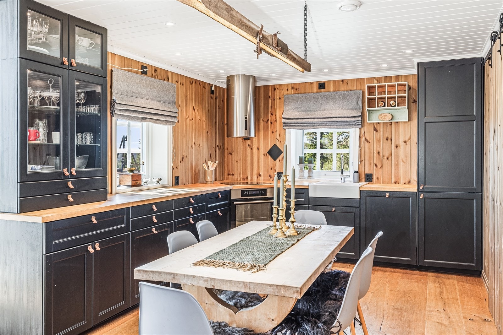 Det romslige kjøkkenet passer fint inn i hyttestilen og vidererfører det lune og moderne preget. Her er det sort innredning med rette profiler og en heltre benkeplate med gode arbedsflater. Galleribilde