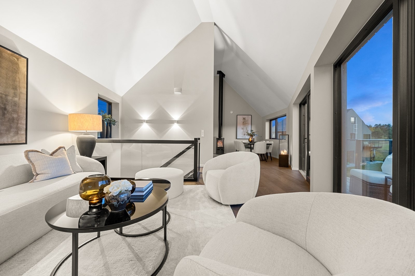 Rommet er åpent mot både spisestuen og kjøkkenet, med store vindusflater innrammet i sort som slipper inn rikelig med lys. Galleribilde