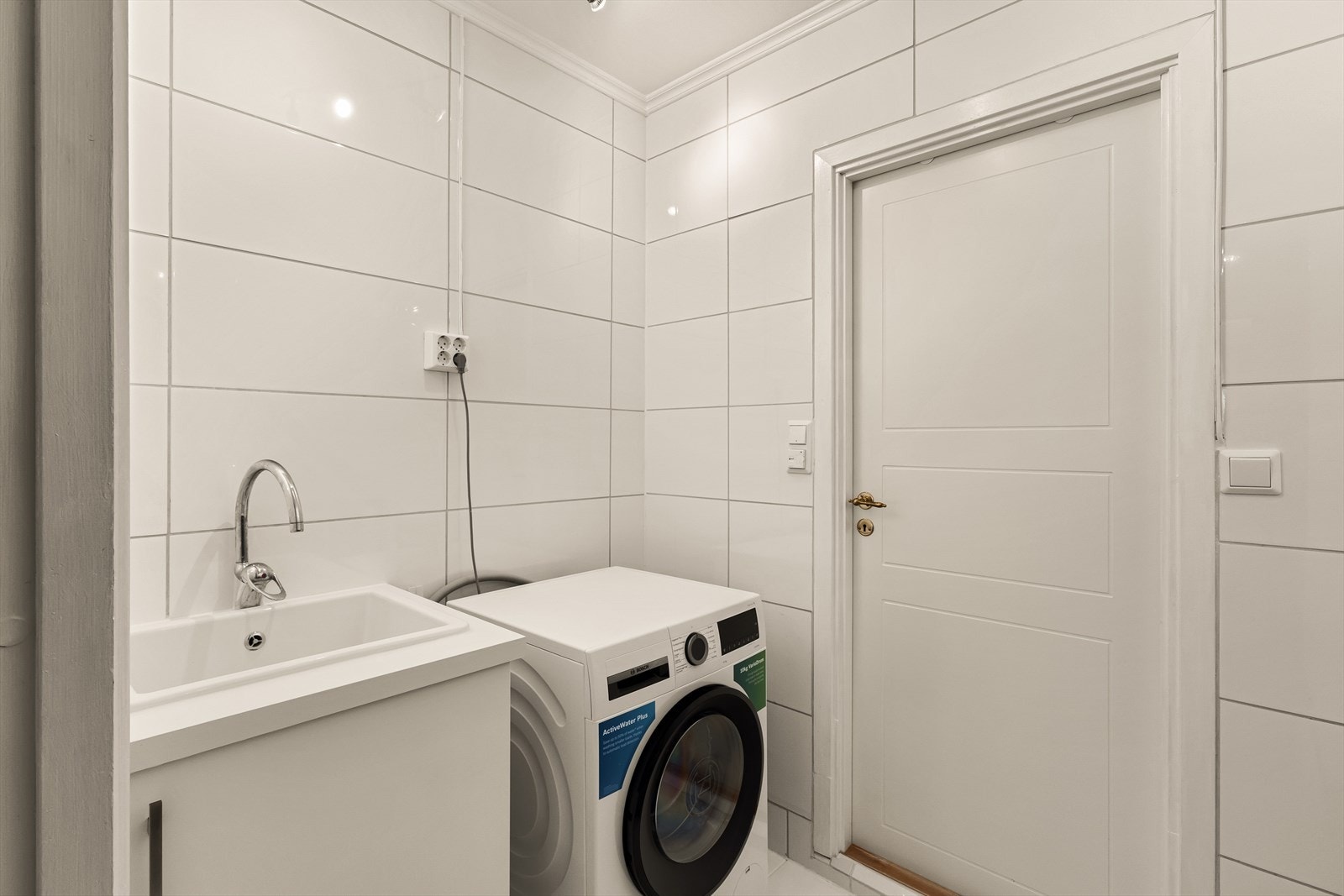 Helfliset vaskerom som inneholder utslagsvask med underskap og opplegg for vaskemaskin Galleribilde