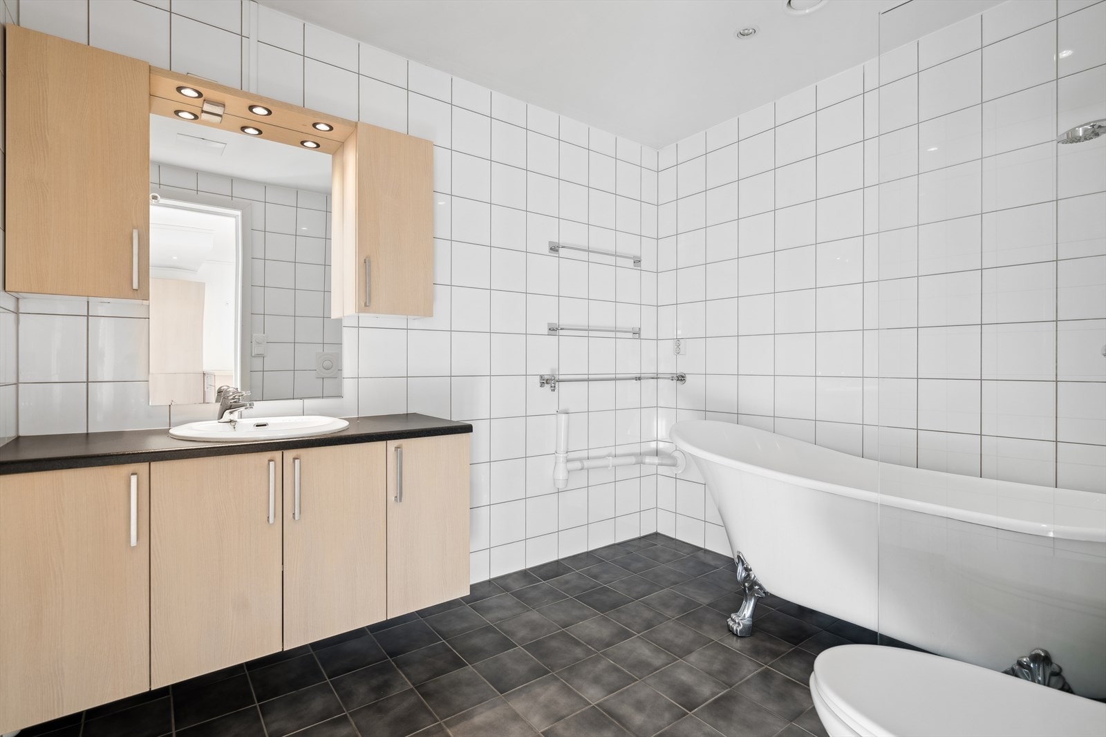 Leilighetens bad har en sentral plassering med enkel tilkomst fra soverommene og stuen. Det er flislagte overflater og behagelig varme i gulvet. Baderomsinnredningen er i samme tidløse stilen som på kjøkkenet. Galleribilde