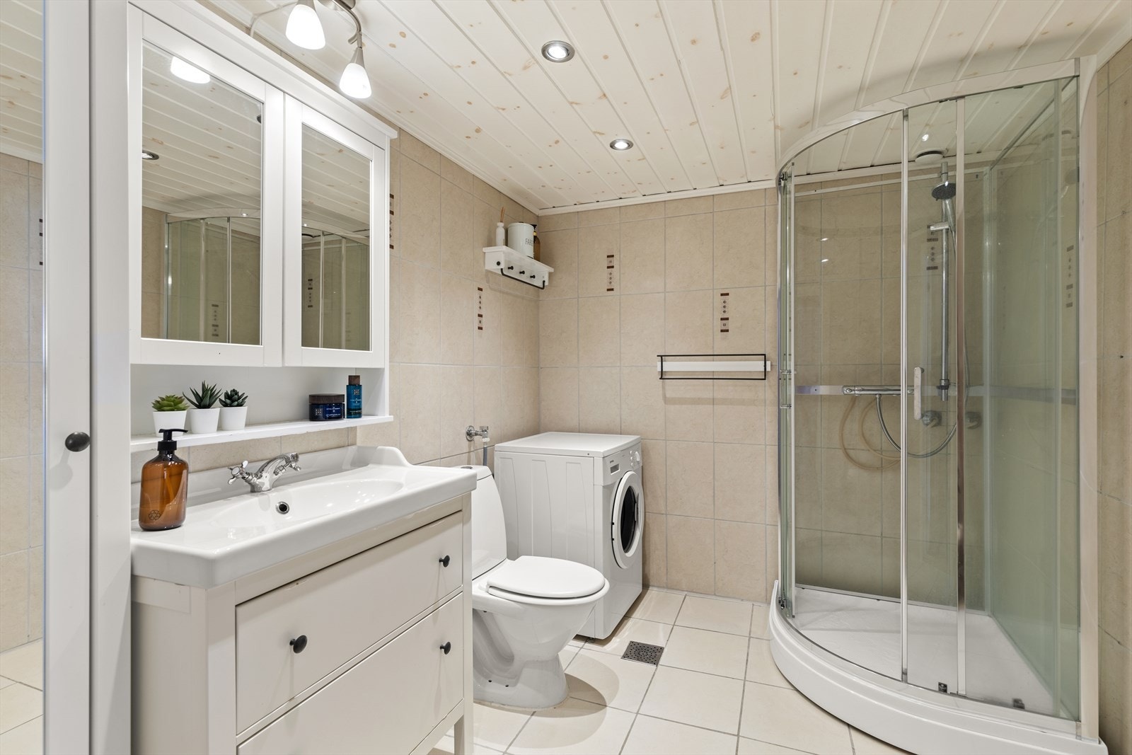 Flislagt bad med innredning med nedfelt servant, toalett, dusjkabinett og opplegg for vaskemaskin. Rommet har elektriske varmekabler. Galleribilde