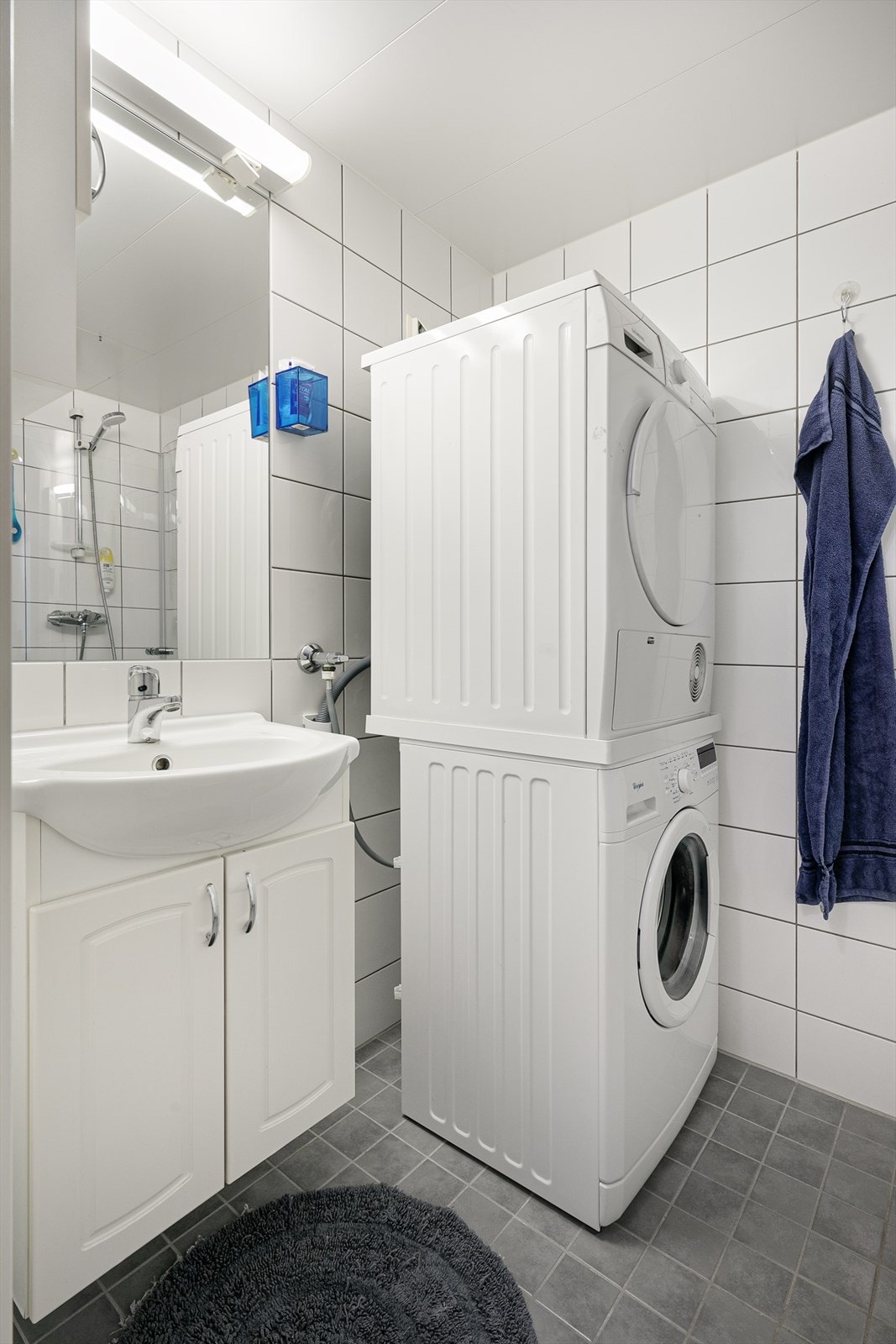 Innredning og garnityr fremstår med veggmonterte dusjdører, servant med underskap, speil og lys, samt veggmontert WC. Galleribilde