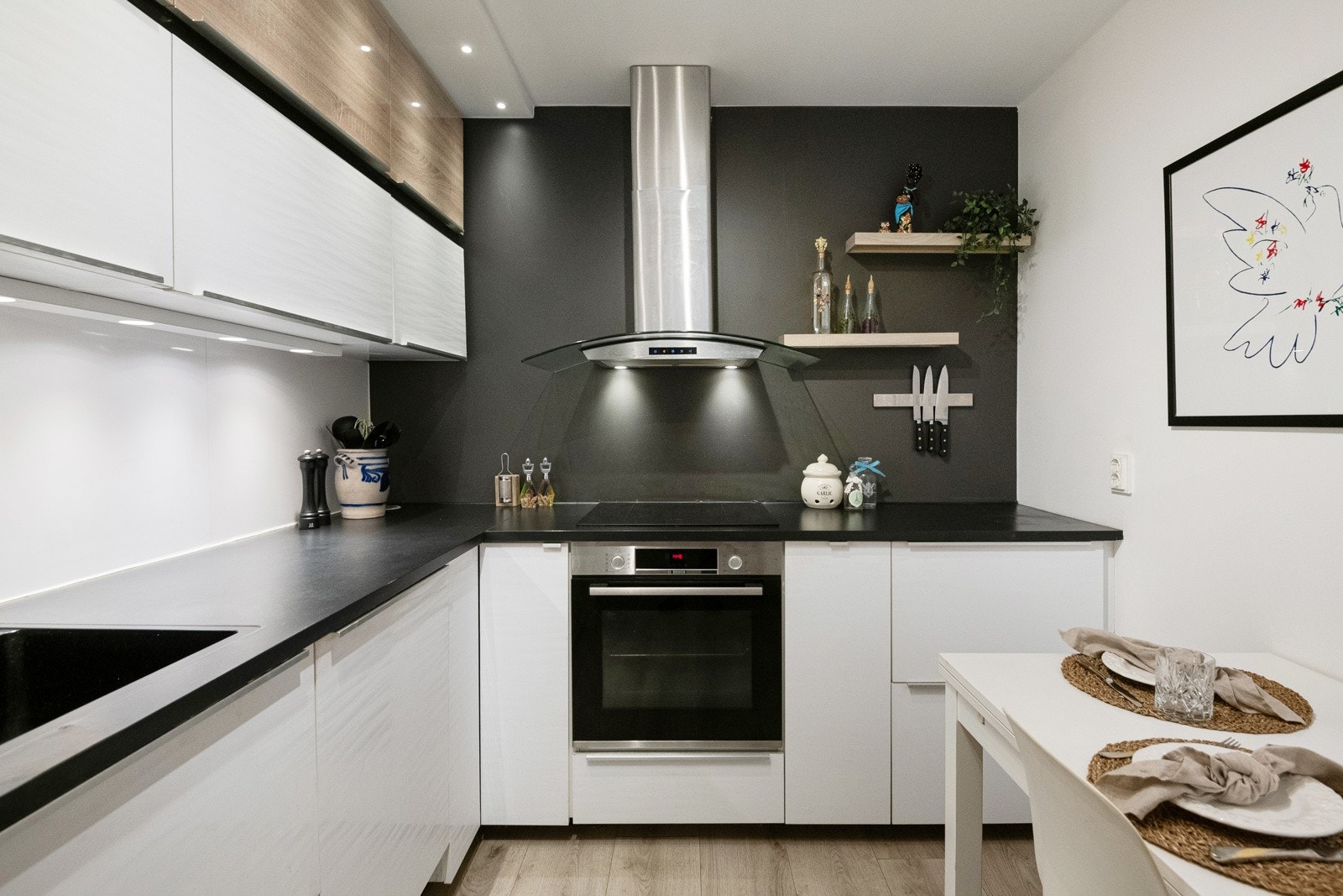 Åpen kjøkkenløsning(2020) med folierte fronter, laminat benkeplate med oppvaskkum, kjøkkenventilator med kullfilter, kitchenboard på vegg over kjøkkenbenk og lys under overskap. Integrert komfyr med induksjonstopp, oppvaskmaskin og kjøl-/fryseskap. Galleribilde