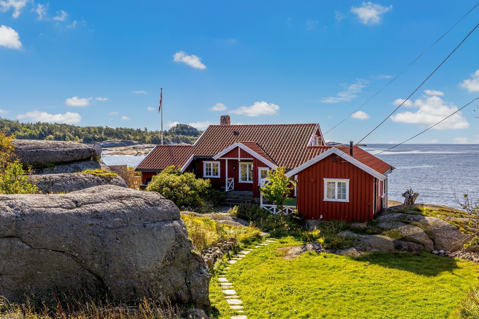 Hytta har adkomst via sti over hagen på nordsiden. Her er det anlagt plen og plantet flere prydbusker. Galleribilde