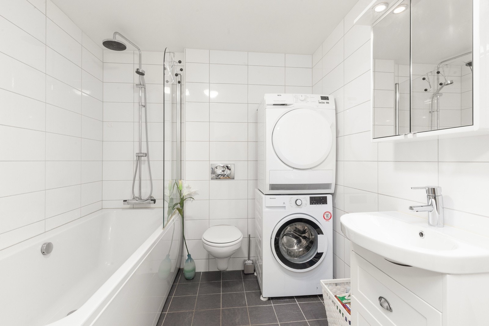 Pent bad med fliser på både gulv og vegger, badet i første etasje er utstyrt med badekar, vegghengt toalett, baderomsinnredning og opplegg til vaskemaskin Galleribilde