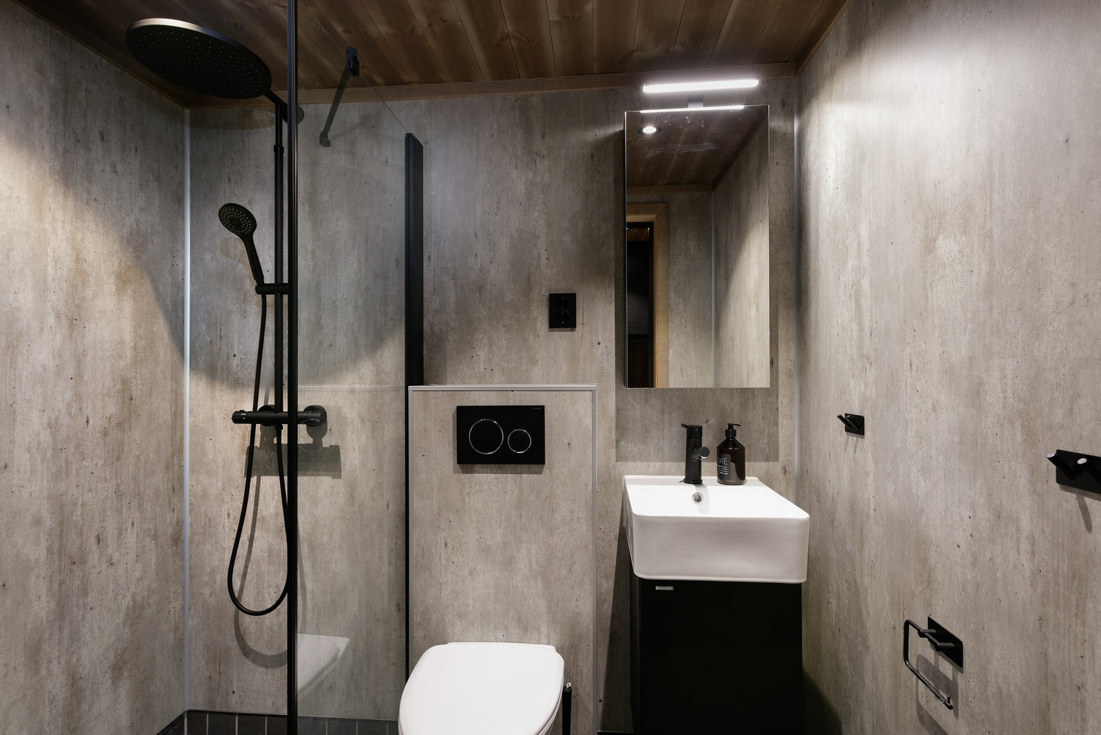 Bad med flislagt gulv, baderomsplater på vegger, servantinnredning, vegghengt toalett og dusjhjørne med glassvegg. Galleribilde