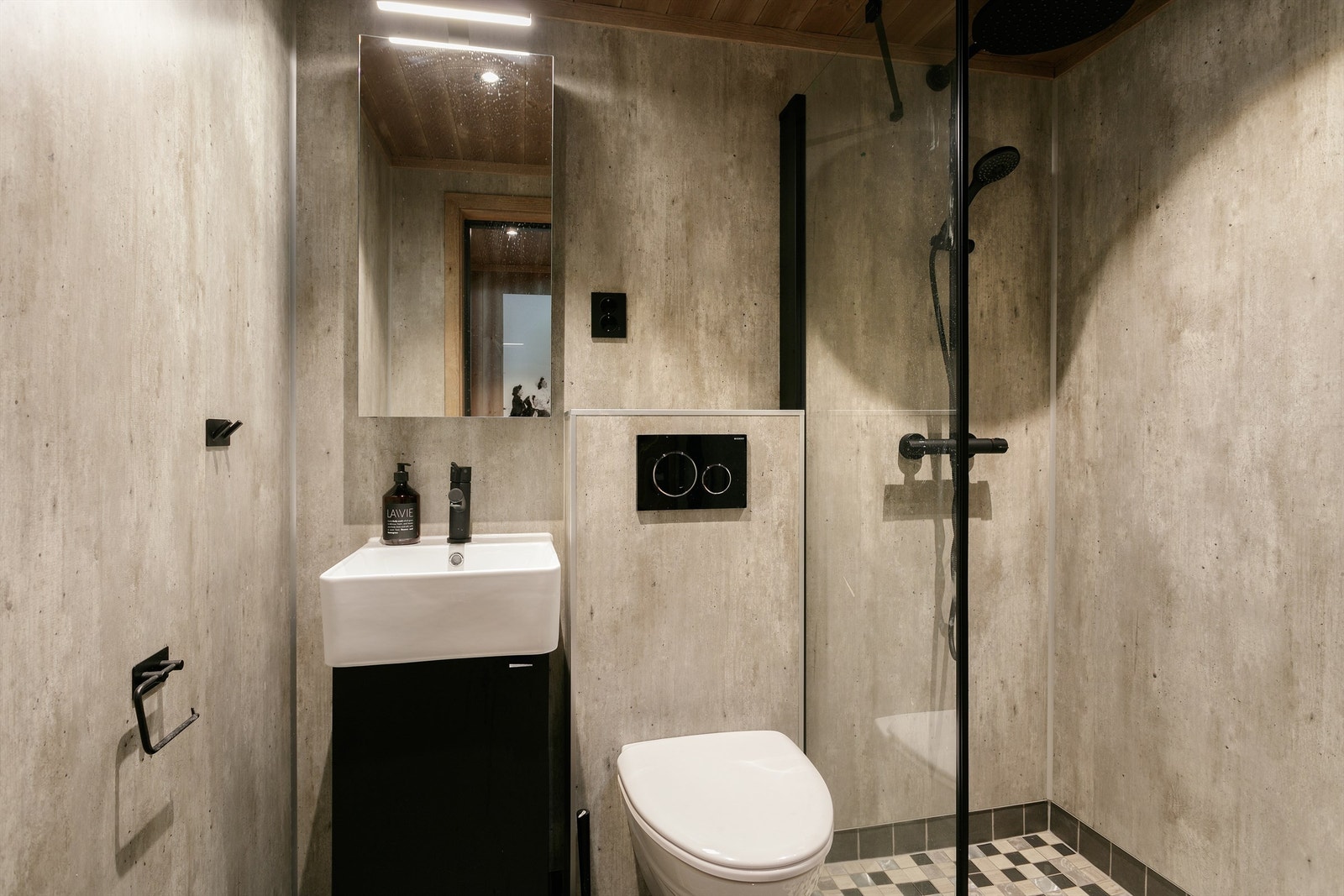 Bad med flislagt gulv, baderomsplater på vegger, servantinnredning, vegghengt toalett og dusjhjørne med glassvegg. Galleribilde