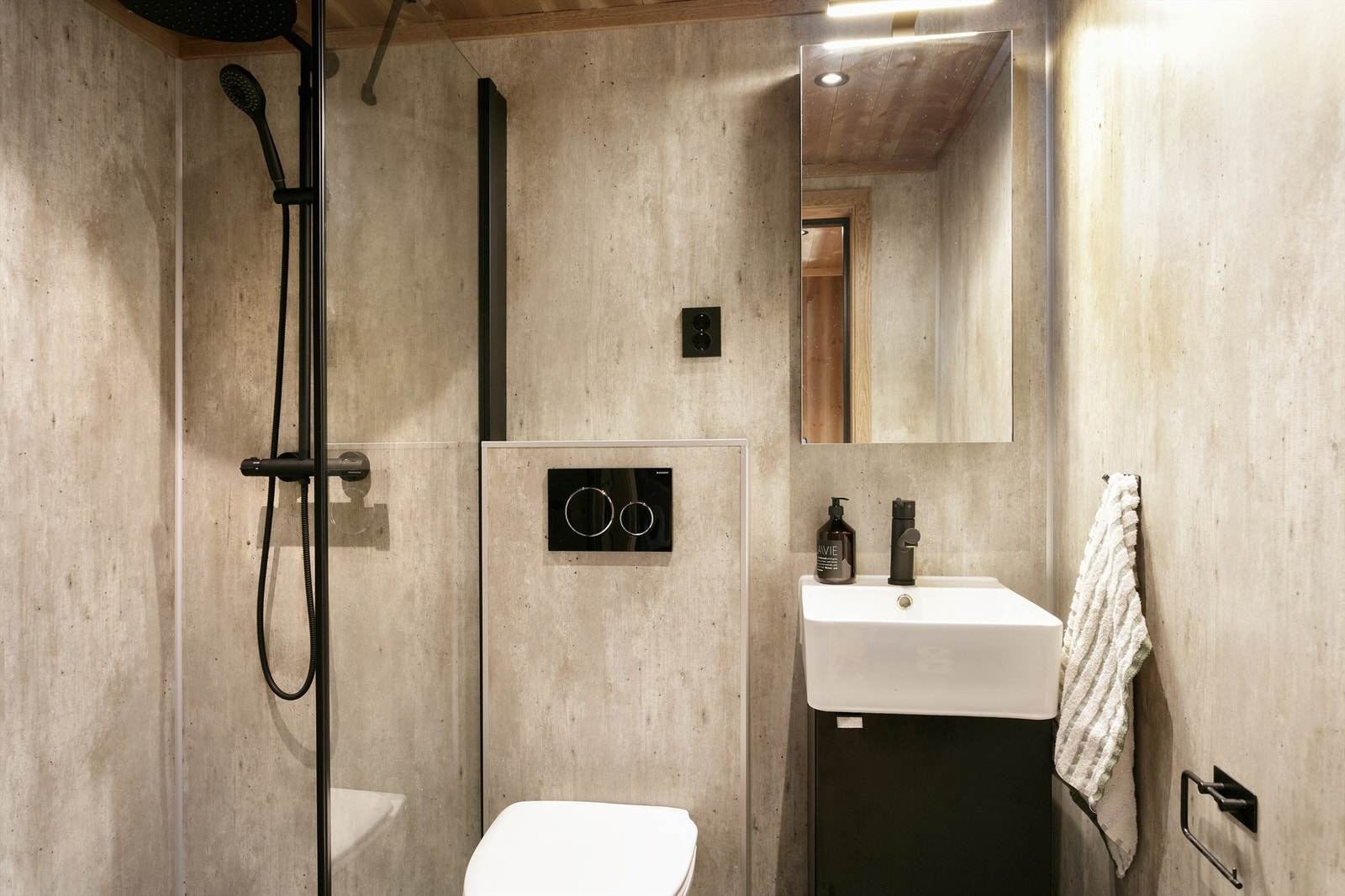 Bad med flislagt gulv, baderomsplater på vegger, servantinnredning, vegghengt toalett og dusjhjørne med glassvegg. Galleribilde