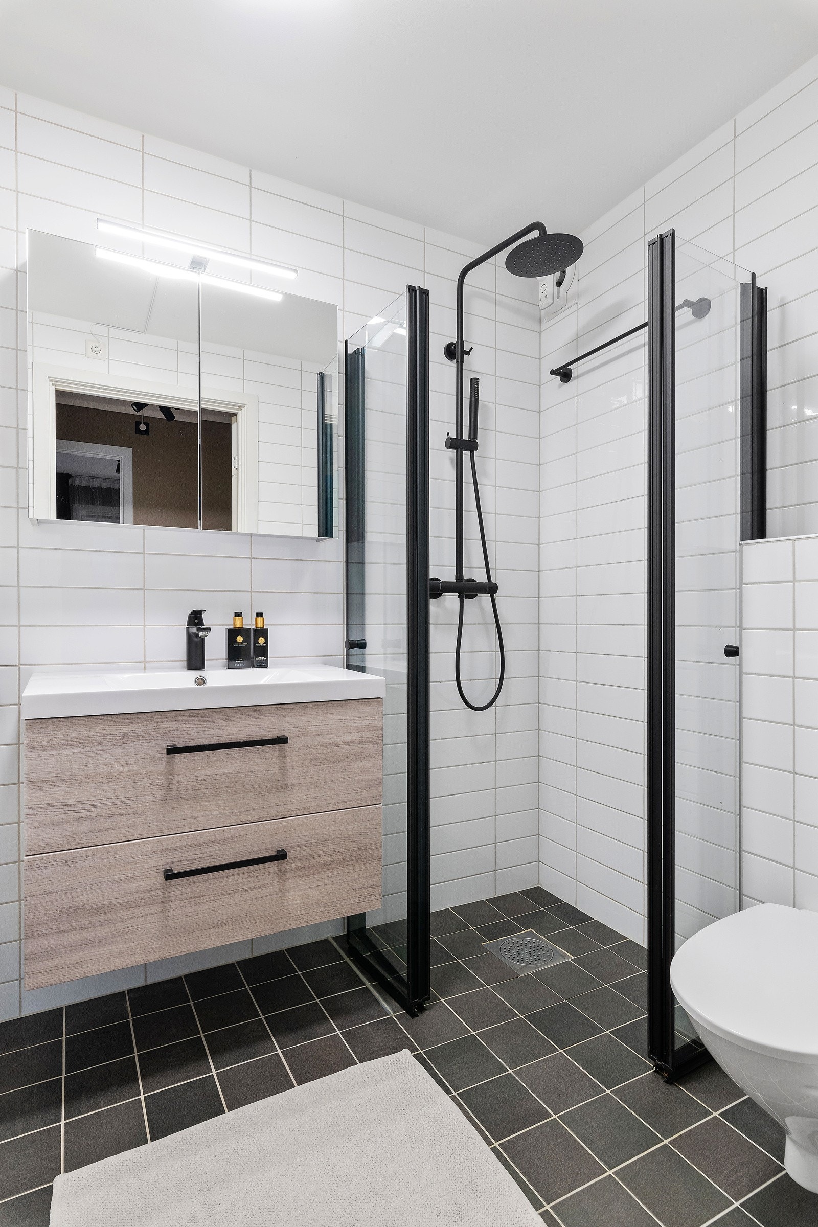 Dusjdørene er skiftet til moderne svart farge. Toalett, servant med innredning og opplegg for vaskemaskin og tørketrommel. Galleribilde