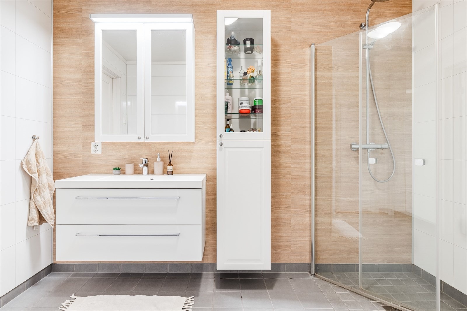 Moderne baderomsinnredning med skuffer og heldekkende servant, speilskap med belysning over, samt ekstra høyskap ved siden av. Galleribilde