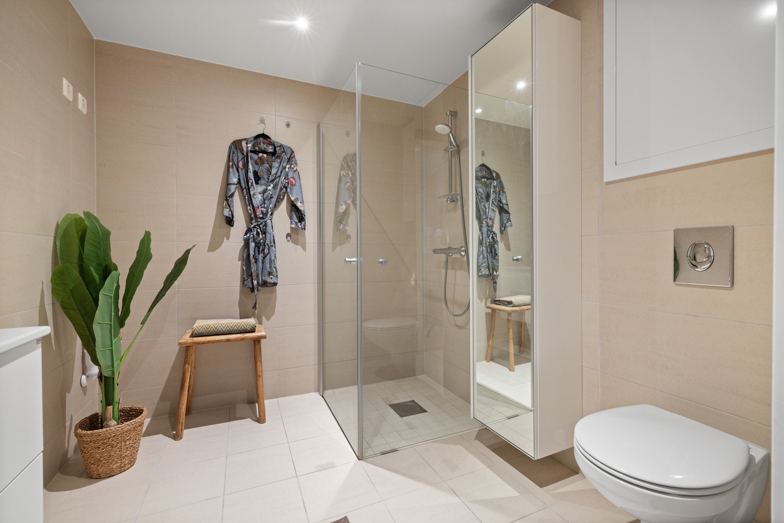 Badet fremstår som moderne og delikat, med beige fliser på veggene, downlights i himlingen og hvite fliser på gulv med gulvvarme. Galleribilde