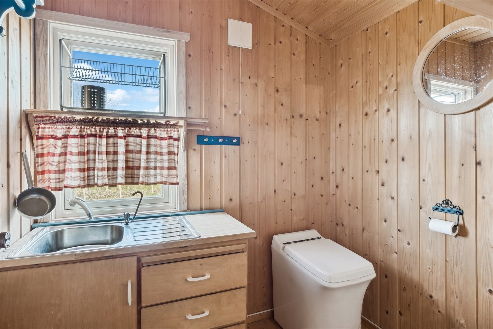 Toalettrom med forbrenningstoalett og enkel innredning med oppbevaringsplass i skuffer og skap, og med vaskekum med gråvann til terreng. Galleribilde