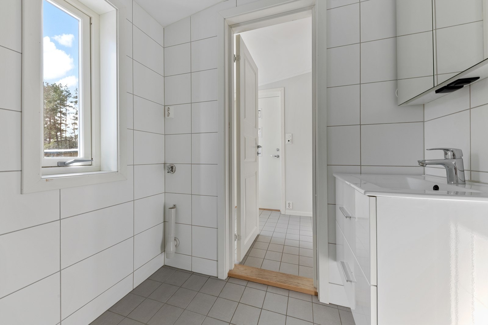 Videre er badet utstyrt med baderomsinnredning med servant og ett-greps blandebatteri, overskap med speil og lys, samt gulvstående toalett og dusjhjørne med glassdører. Det er opplegg for vaskemaskin på badet og gulvvarme i gulv Galleribilde