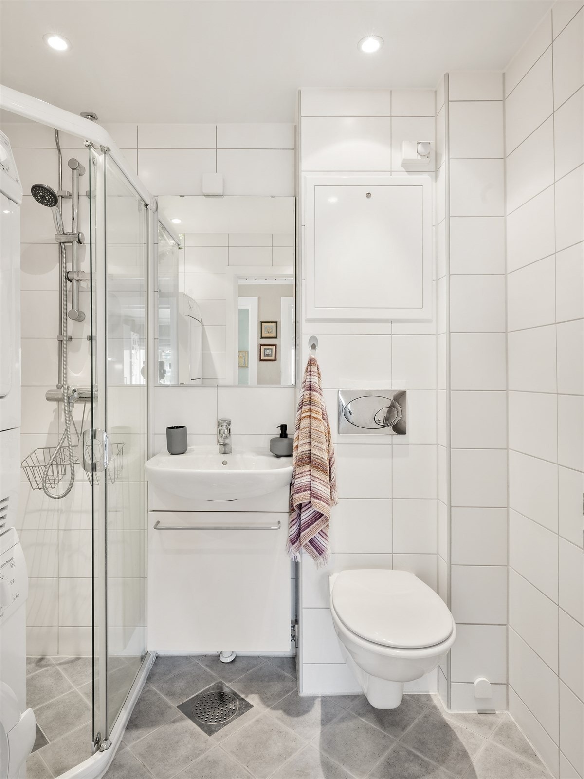 Moderne flislagt bad utstyrt med dusj, stilren servant og vegghengt toalett. Galleribilde