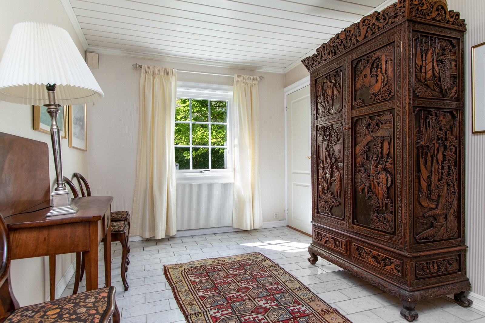 Hovedentreen er representativ og romslig med lyse marmorfliser på gulvet, stripete tapet på veggene og hvitmalt paneltak. Galleribilde