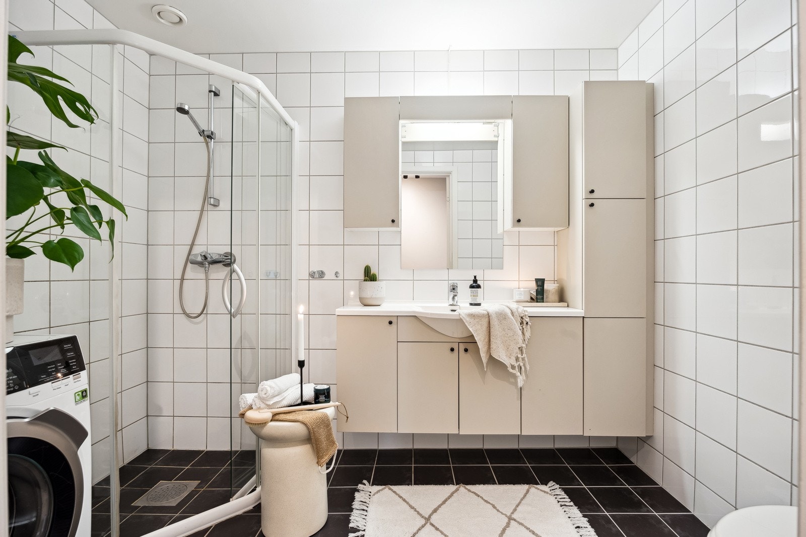 Flislagt baderom utstyrt med vegghengt toalett, dusjhjørne, vegghengt servantinnredning og skap. Galleribilde