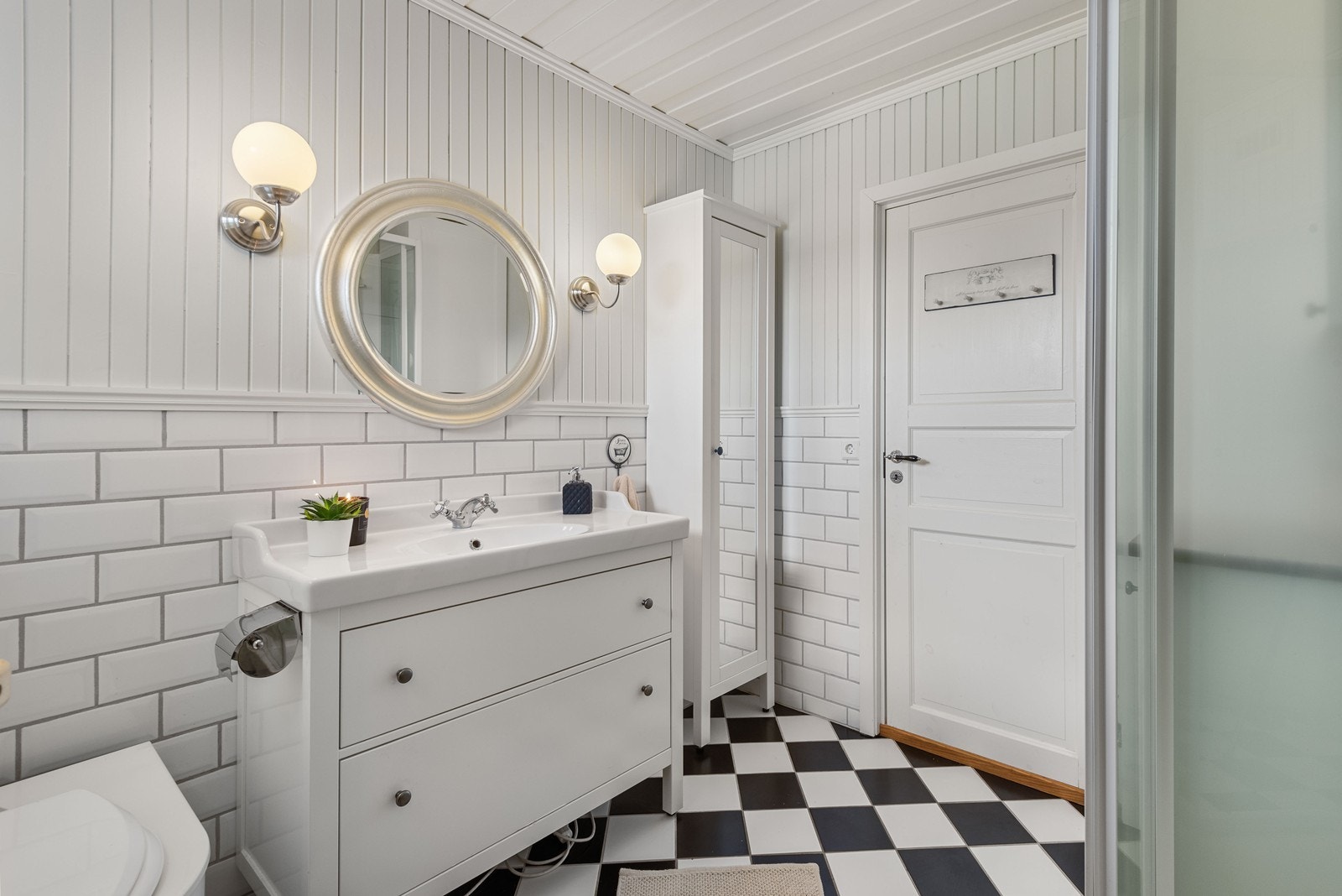 Badet fremstår lyst og tidløst, med flislagt gulv i sjakkmønster og delvis flislagte vegger. Galleribilde
