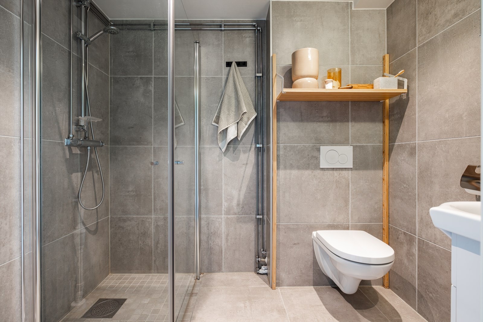 Pent flislagt baderom med romslig dusjhjørne med innfellbare glassvegger, vegghengt klosett, servantinnredning samt opplegg og plass til vaskemaskin. Galleribilde