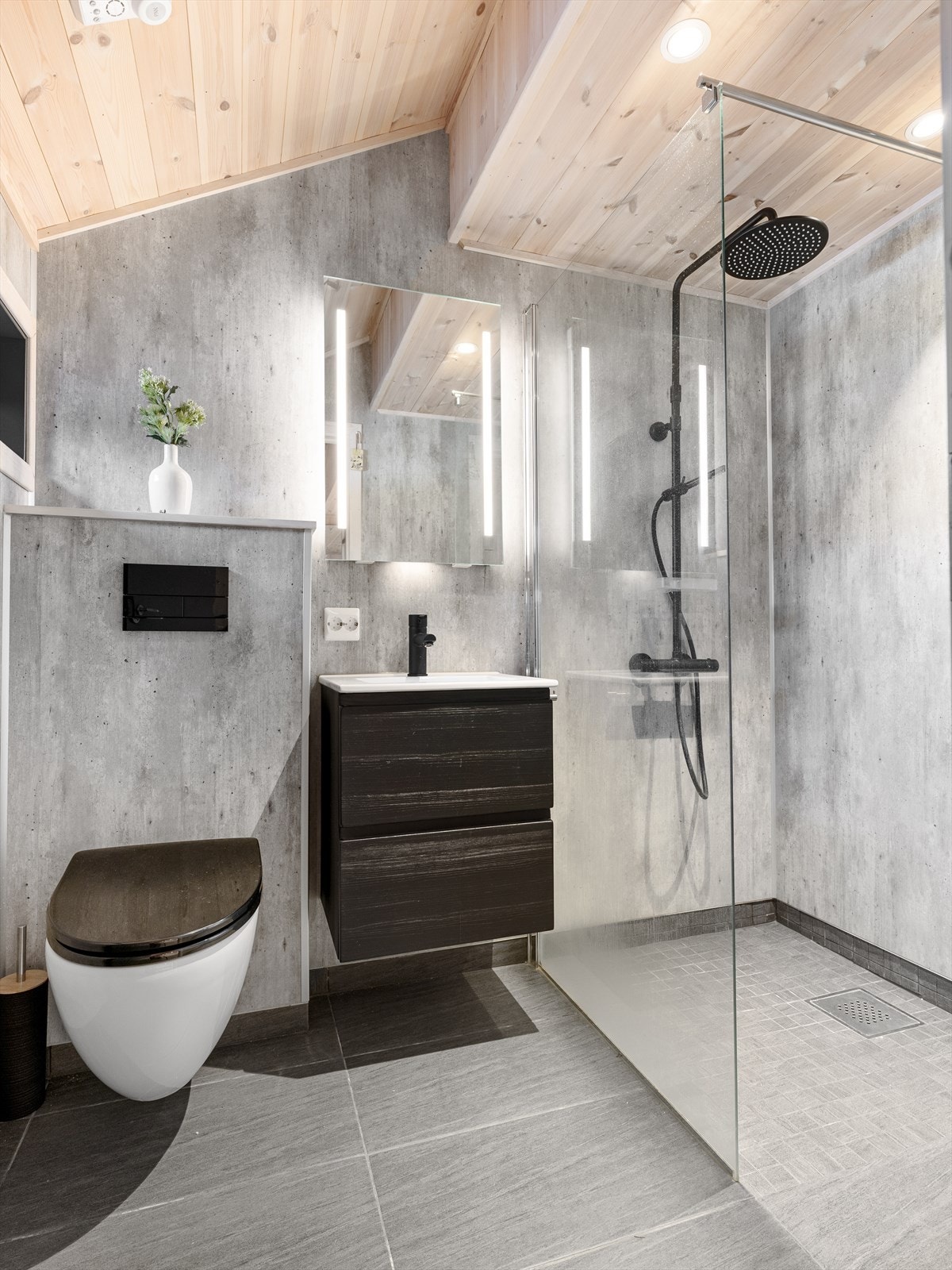 Bad med fliser på gulv med varmekabler under. Våtromsplater på veggene. Dusj med glassvegg, Vask i seksjon og speil med belysning. Vegghengt wc. Spotter i tak. Galleribilde