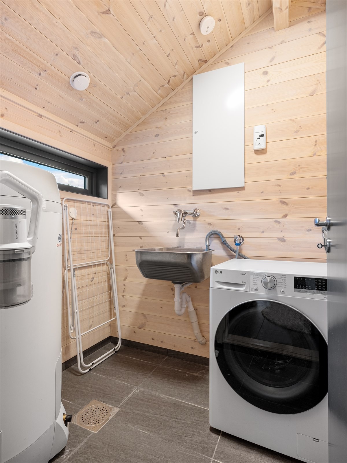 Vaskerom med utslagsvask, opplegg for vaksemaskin og varmtvannsbereder. Fliser på gulv. Galleribilde