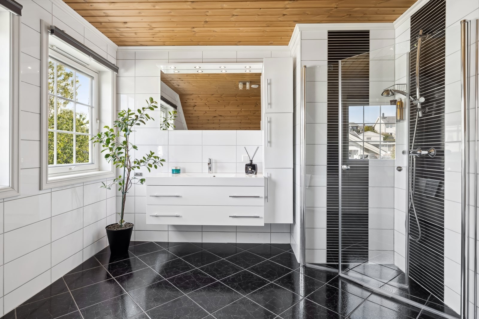 Badet er videre utstyrt med speil med downlights på vegg over servanten, dusjhjørne med glassdører, sluk i sone og dusjutstyr, samt badekar med dusjutstyr og wc. Galleribilde