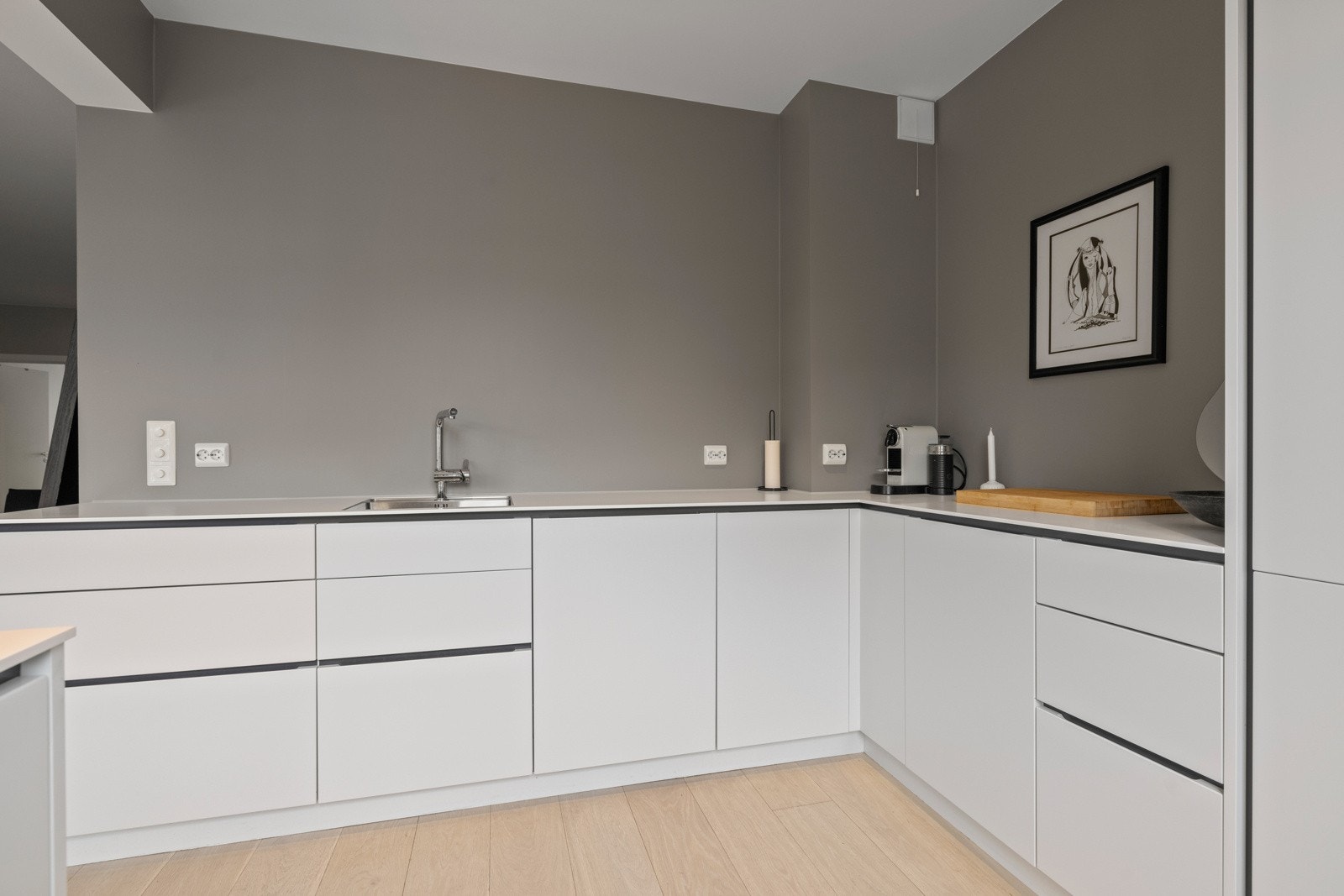 Innredningen består av hvite grepsfrie fronter, hvit benkeplate i kompakt laminat med underlimt vask og ett-greps armatur i krom samt integrerte hvitevarer Galleribilde