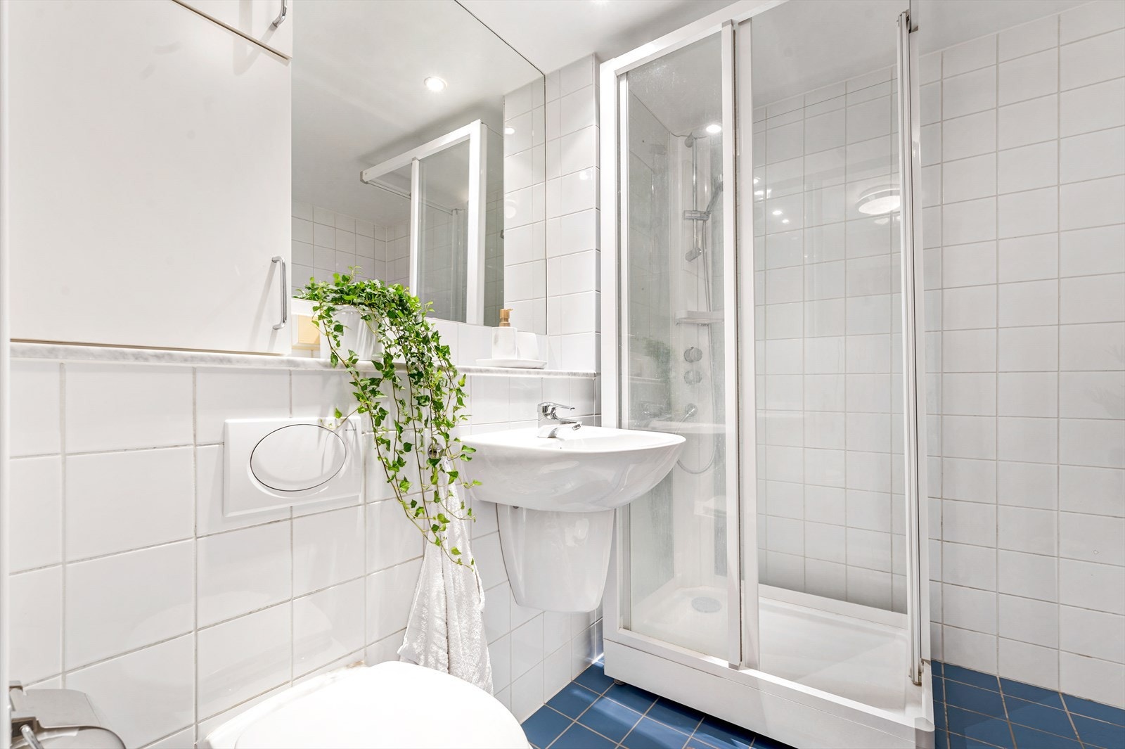 Badet er innredet med vegghengt toalett, servant, veggskap og et nyere dusjkabinett. Galleribilde