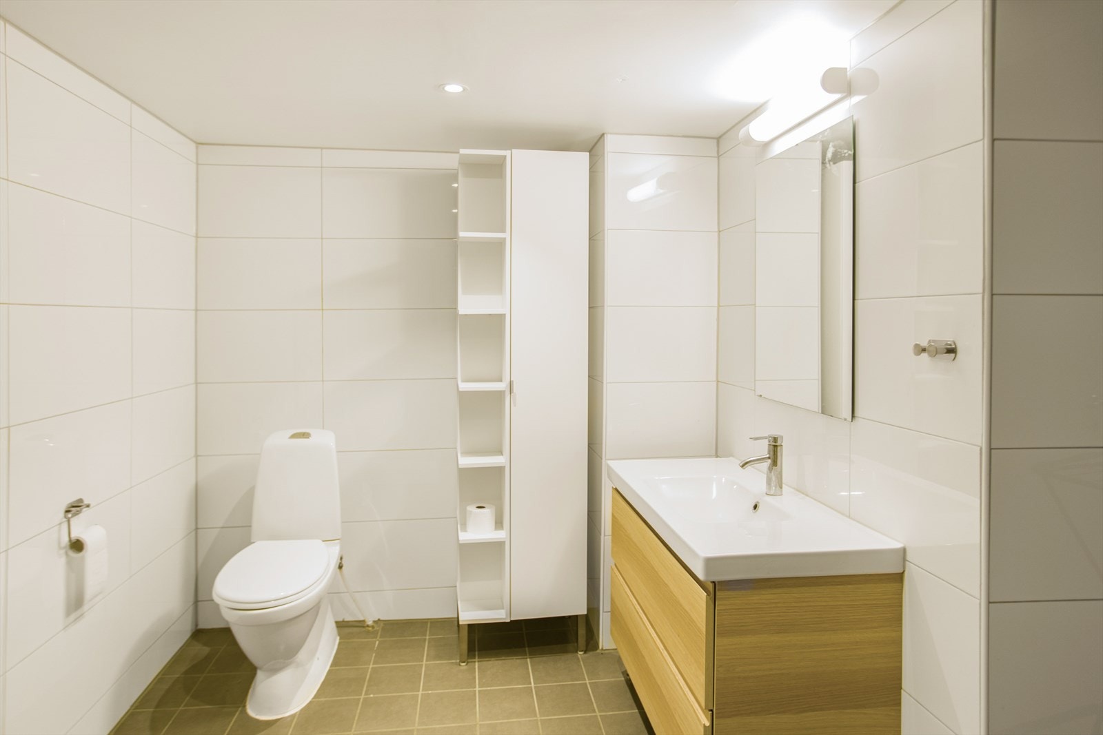 Baderom fra 2017. Baderommet er innredet med servant med underskap, speil med tilhørende belysning, dusjkabinett, gulvmontert toalett og opplegg for vaskemaskin. Galleribilde