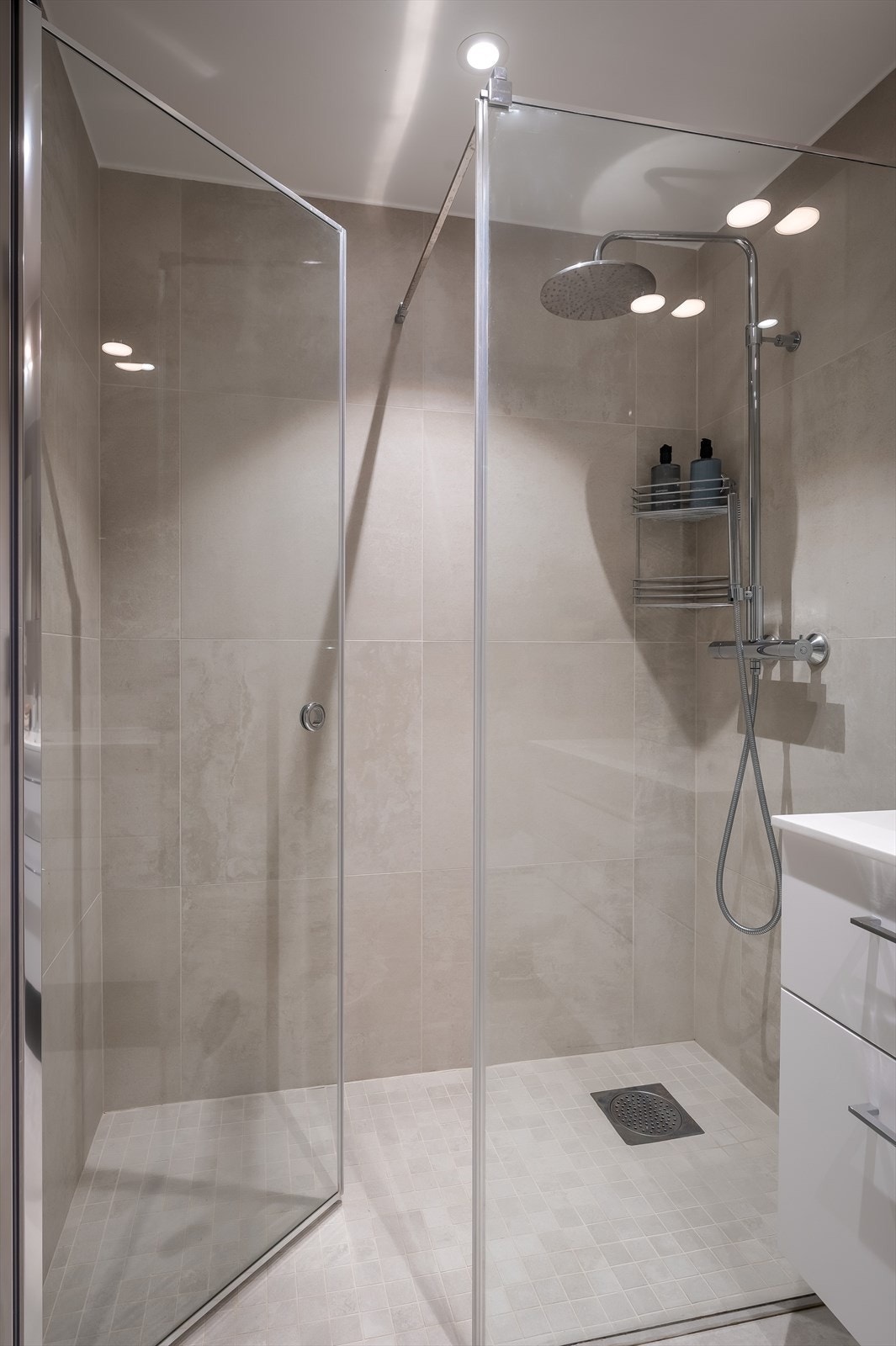 Badet er innredet med servant med skuffer, speilskap med belysning, veggmontert klosett, og dusjhjørne med glassdører. Galleribilde