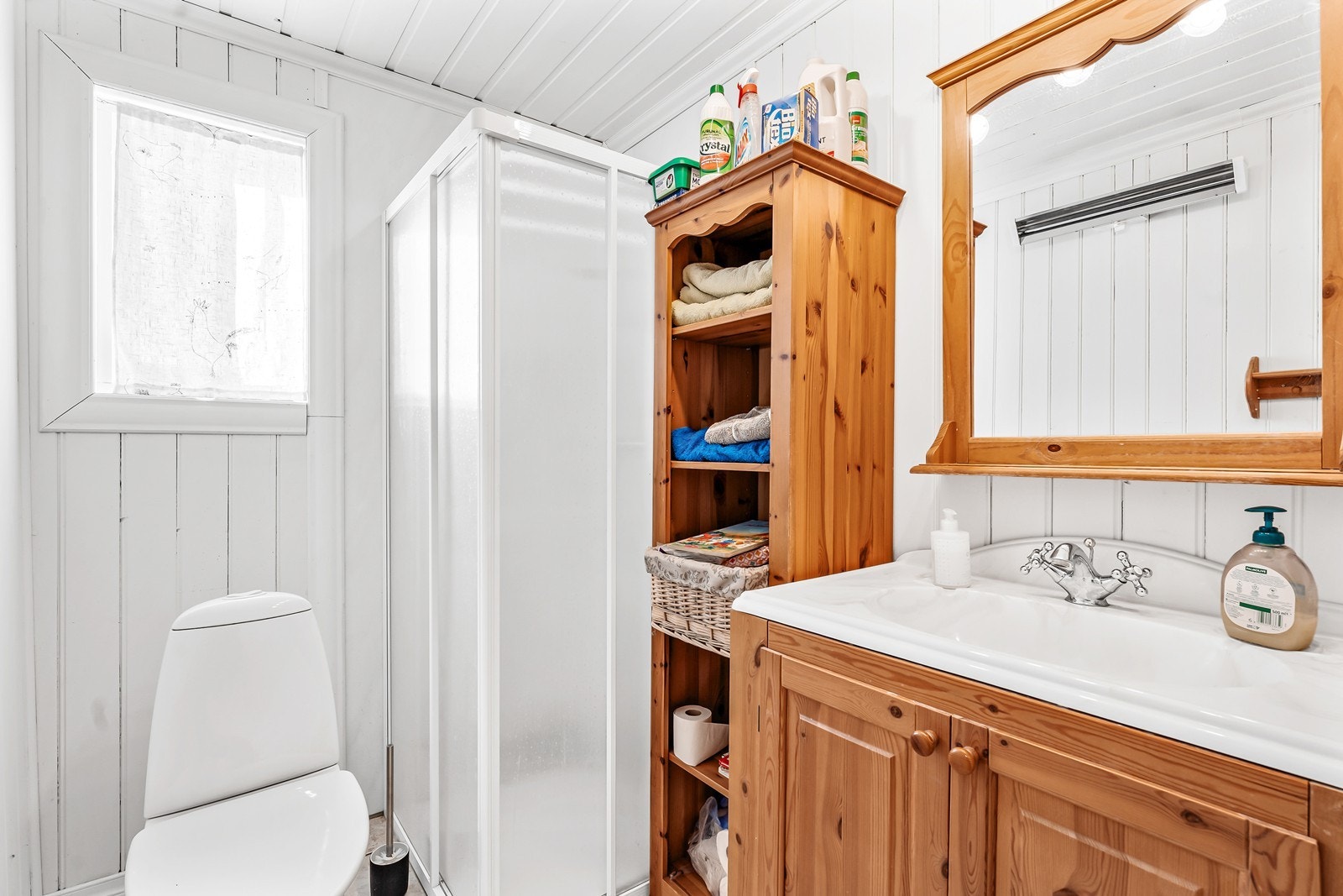 Boligens bad har panel på vegger og keramiske fliser på gulv., videre innredet med servant i baderomsmøbel, toalett og dusjsone. Galleribilde