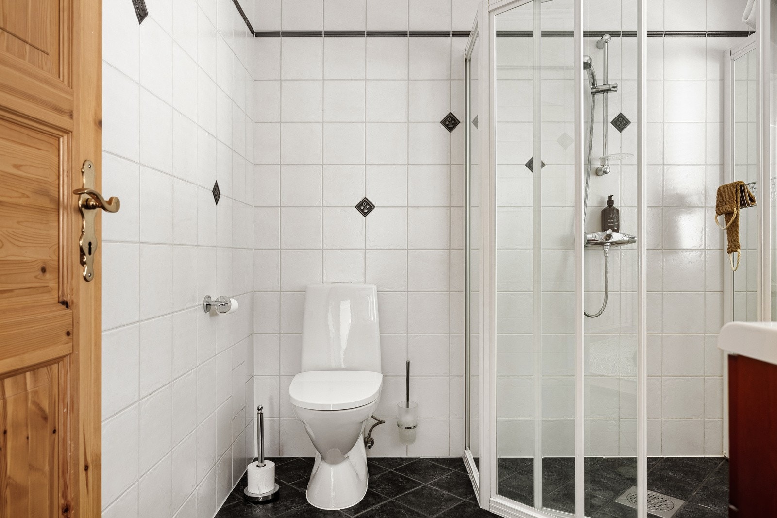 Badet er helfliset og innredet med vegghengt servantinnredning, vegghengt toalett, dusjhjørne og speil med belysning. Galleribilde